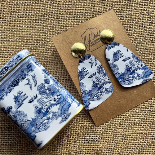Blue Willow patterned earrings on a matching pouch with a brown card on a textured brown background