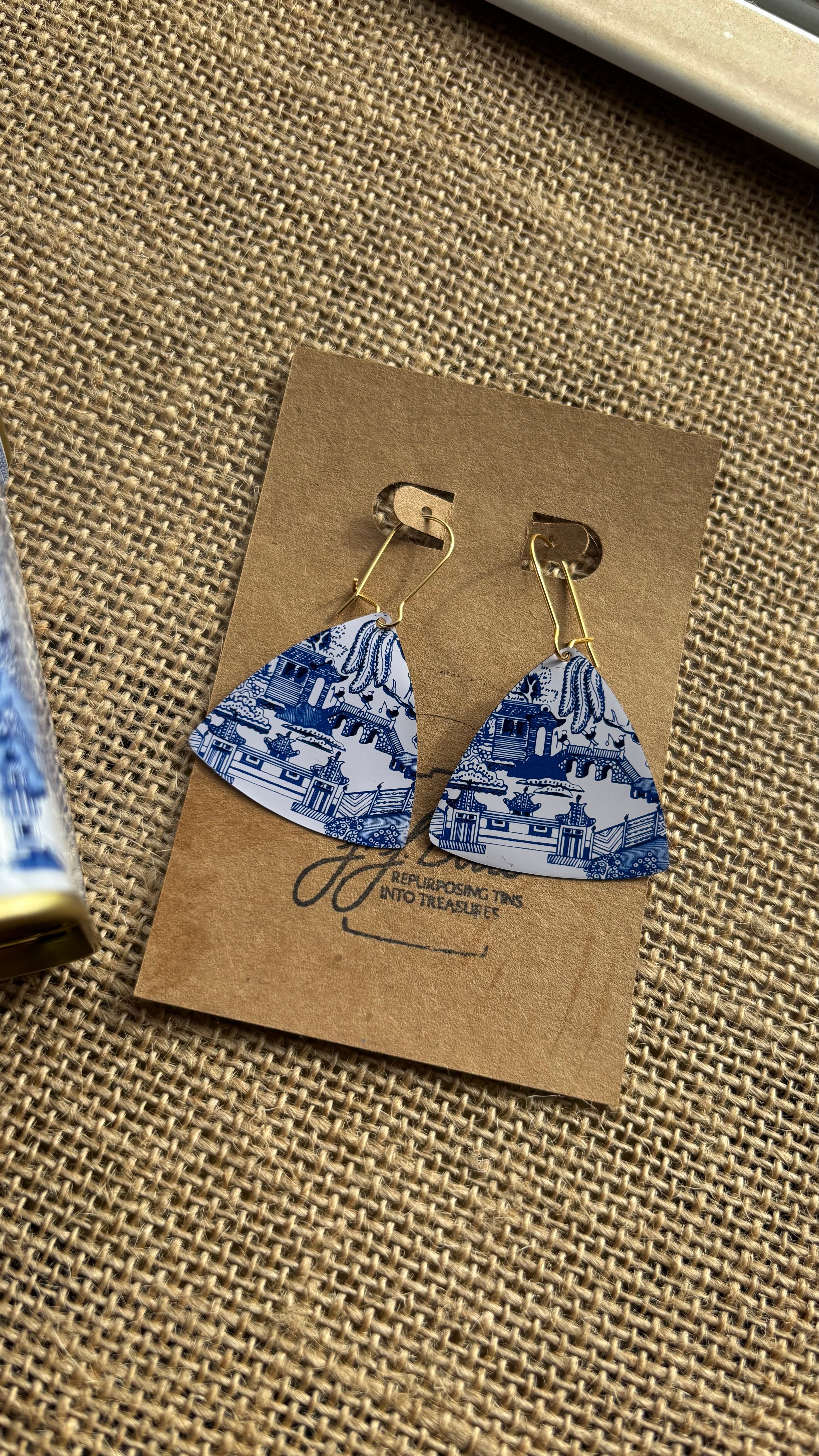 Triangular earrings with blue and white pattern on a brown card with brand name.